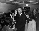 "Lyndon B. Johnson taking the oath of office aboard Air Force One at Love Field Airport two hours and eight minutes after the assassination of John F. Kennedy"